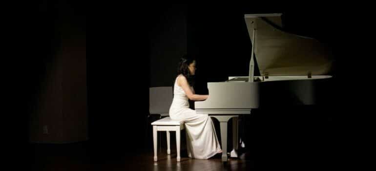 Woman in white dress playing the piano after the relocation with piano movers Austin.