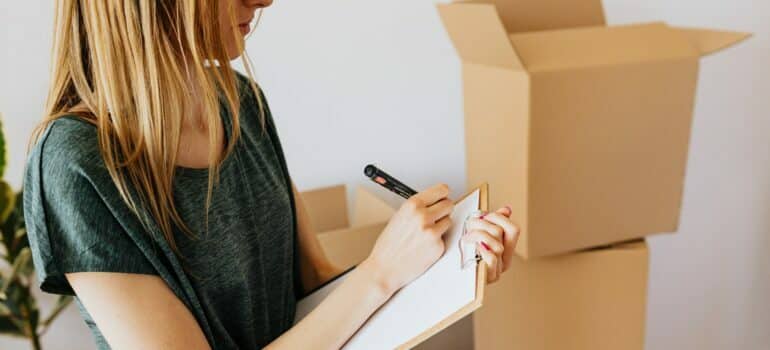 woman taking notes in clipboard near carton boxes