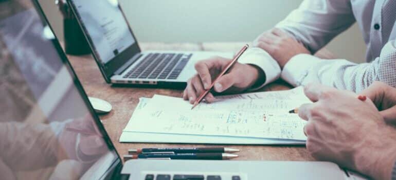 two laptops and a hand with a pan writing 