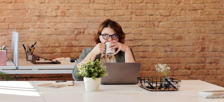 woman sitting in front of the laptop, thinking, drinking coffee