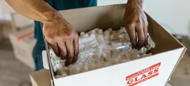 professionals packing glassware in the cardboard box filled with packing peanuts