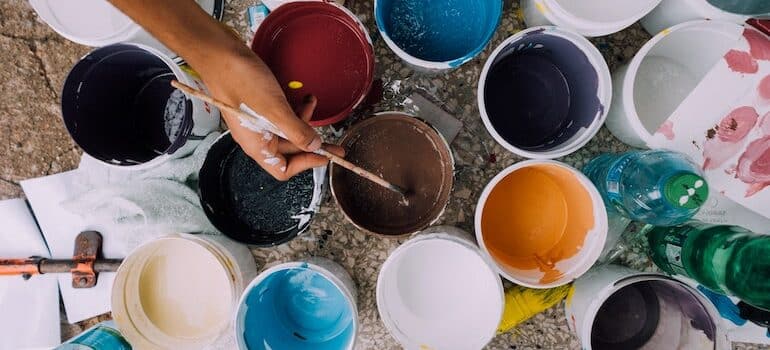 a lot of buckets with paints and a hand holding a brush