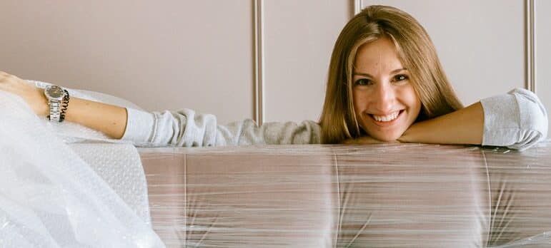 a woman sitting behind a couch covered in plastic wrap