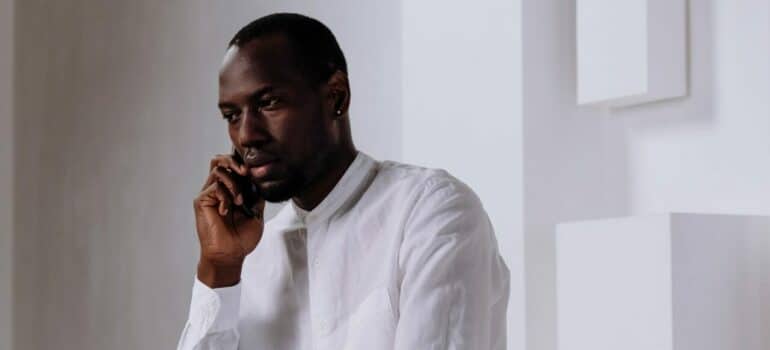 a man in a white shirt sitting while talking on the phone