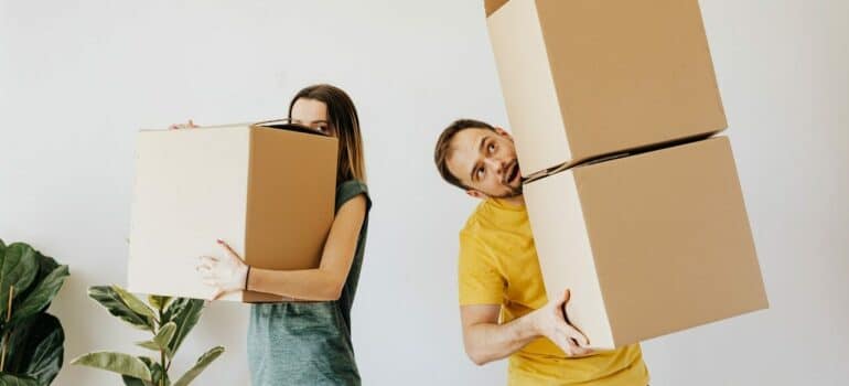 a man and a woman holding cardboard boxes as the main leftover packing materials after a move