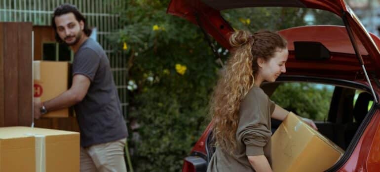 a couple placing cardboard boxes in their car to prepare for the road