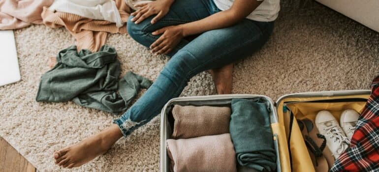 a girl packing clothes in a suitcase, while sitting on the floor