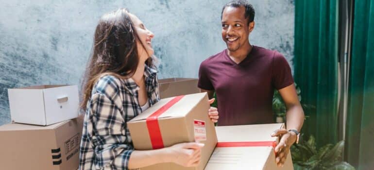 a woman laughing with a person from the moving crew as they handle cardboard boxes
