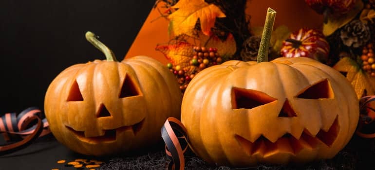 Pumpkins with scary faces are stacked upon each other on a pile.