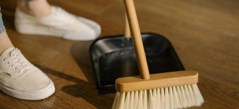 a woman cleaning a wooden floor with a broom as one of the after-holiday cleaning tips