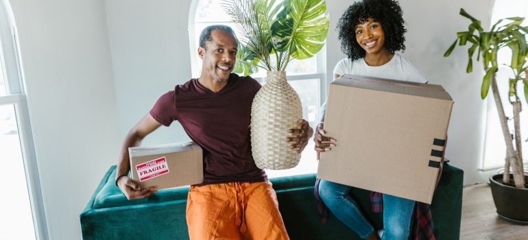 A pair holding a plant and boxes, and posing.