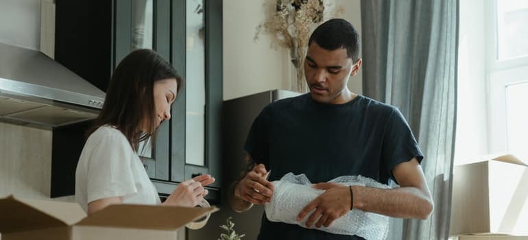 Man bubble wrapping and woman opening a new tape, before moving into a new home in South Austin;