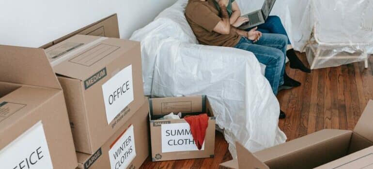 a couple sitting on the couch near brown cardboard boxes