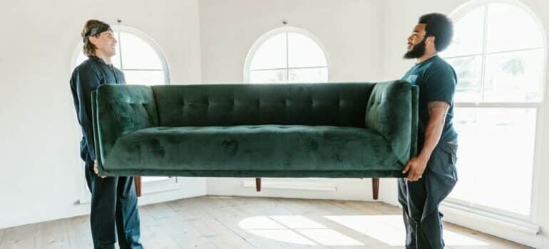 Two professional movers carrying large sofa can help you decide between DIY moving vs hiring Westlake movers