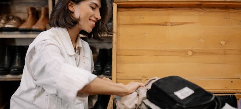 Woman in white jacket sitting by the wooden box with clothes.