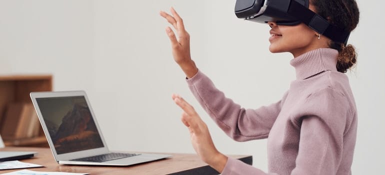 A woman wearing a VR goggles in front of the laptop;