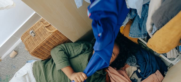Black girl lying on stack of clothes in bedroom