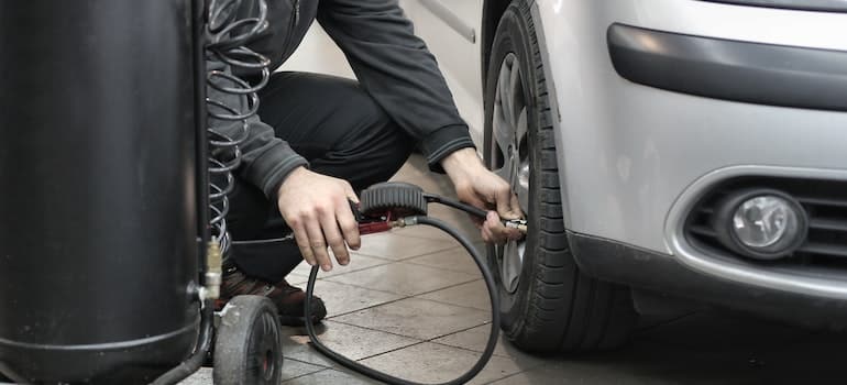 Man in Black Jacket and Black Pants Sitting Near Silver Vehicle.
