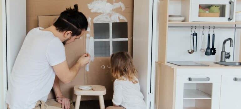 Father and daughter painting cardboard house