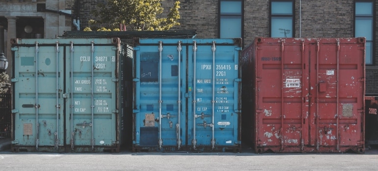 Three shipping containers in front of a building.
