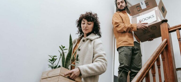Two people carrying boxes down the stairs